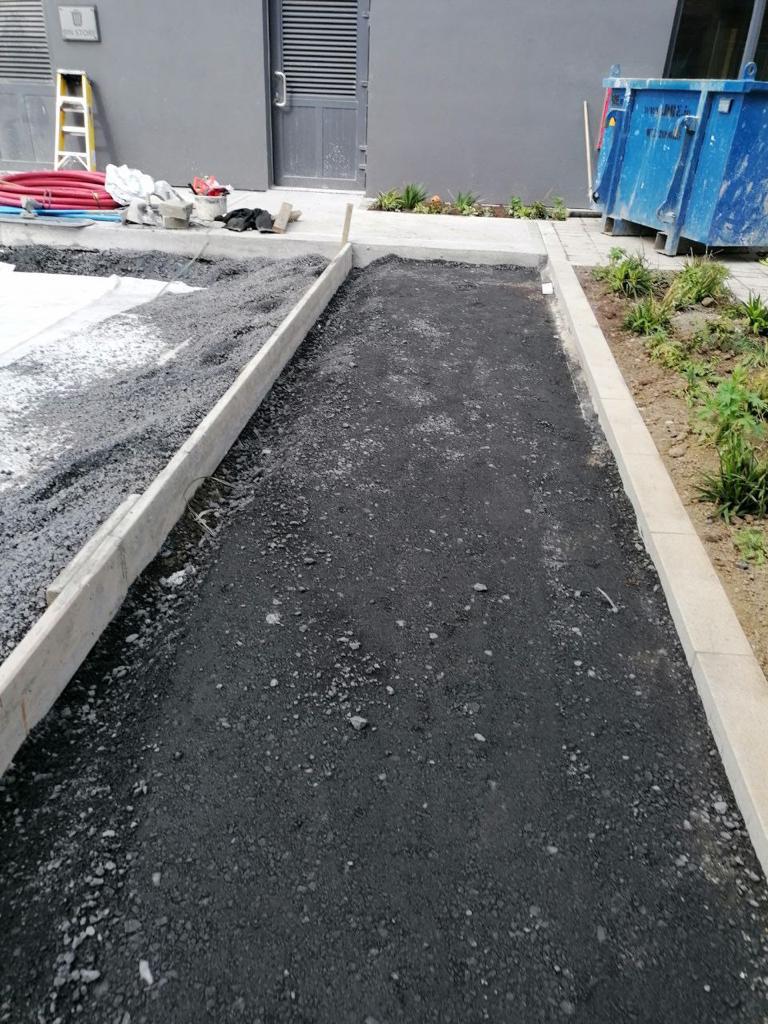 An asphalt walkway with a concrete curb and a garden bed in a construction site